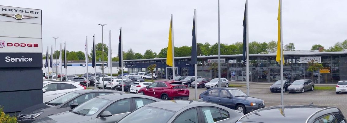 Autohaus Peter in G&ouml;ttingen mit gro&szlig;er Fahrzeugausstellung, sichtbaren Markenlogos von Jeep, Chrysler, Dodge und Opel sowie zahlreichen Flaggen.