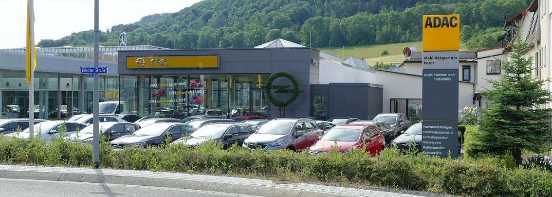 Autohaus Peter als ADAC-Mobilit&auml;tspartner am Standort Sondershausen (Erfurter Stra&szlig;e 41). Im Vordergrund zahlreiche geparkte Autos, rechts ein ADAC-Schild mit gelber Spitze, links das Opel-Logo und ein modernes Autohaus-Geb&auml;ude mit Glasfassade, dahinter gr&uuml;ne H&uuml;gel.