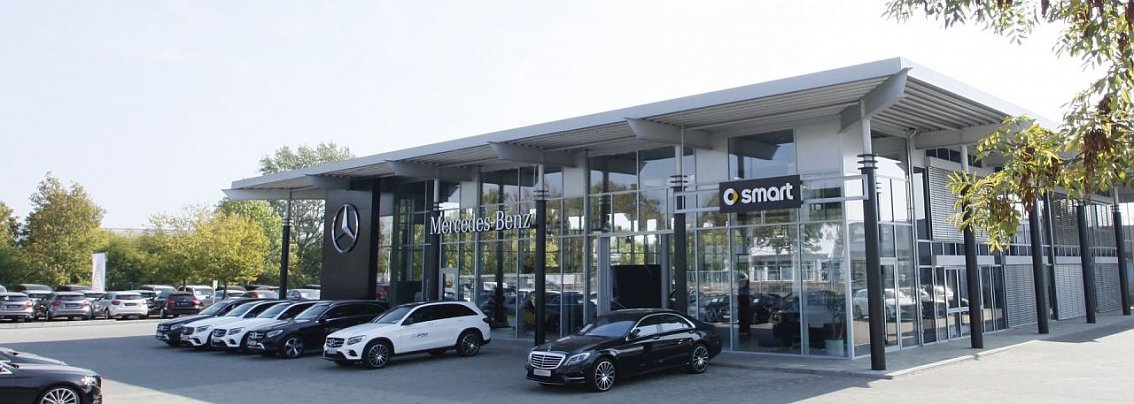 Modernes Mercedes-Benz und Smart Autohaus mit gro&szlig;er Glasfassade in Dessau, davor mehrere geparkte Fahrzeuge, darunter wei&szlig;e und schwarze Autos.