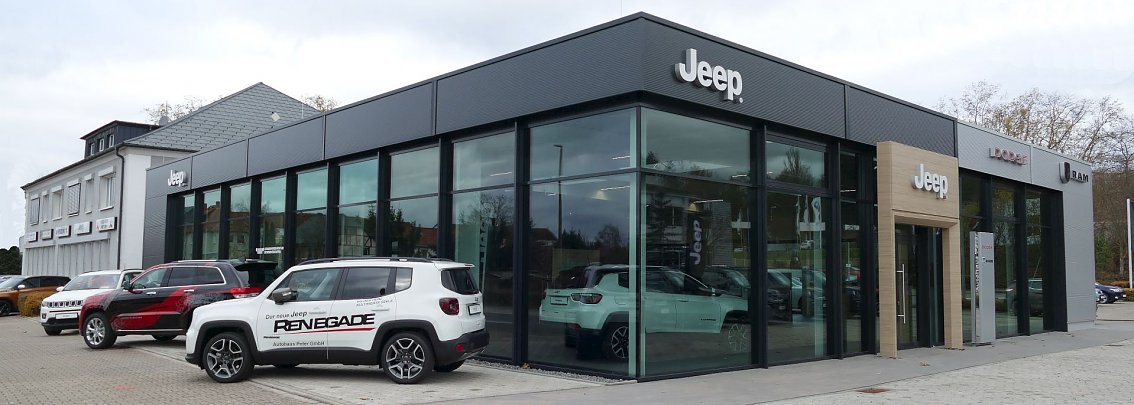 Modernes Jeep-Autohaus in Nordhausen mit gro&szlig;en Glasfassaden, mehreren geparkten Jeep-Fahrzeugen, darunter ein wei&szlig;er Jeep Renegade mit Schriftzug.