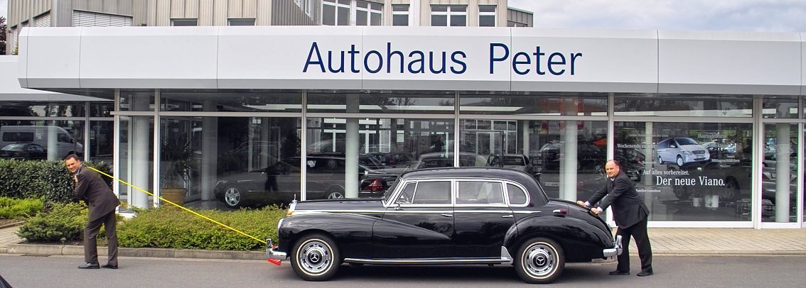 Symbolisches Bild von Helmut Peter und Sohn Andreas Peter und einem historischen schwarzen Mercedes vorm Autohaus Peter. Andreas Peter zieht den Wagen, w&auml;hrend ihn Helmut Peter anschiebt.