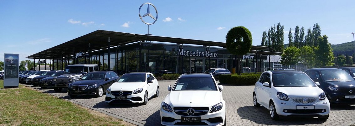 Moderner Mercedes-Benz- und Smart-Standort der Autohaus-Peter-Gruppe in Northeim mit Glasfassade, gro&szlig;em Mercedes-Stern auf dem Dach und einer Reihe neuer Fahrzeuge (darunter Limousinen und Smart-Modelle) auf dem Vorplatz.