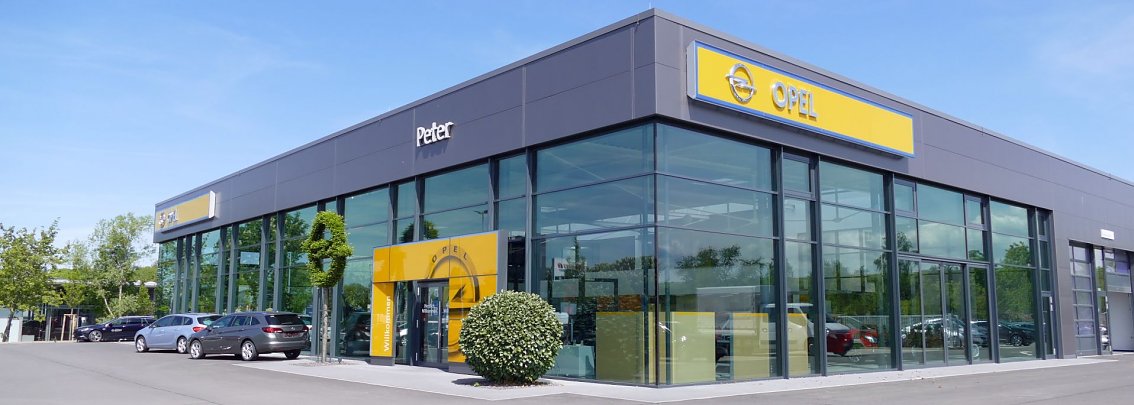 Modernes Autohaus der Marke Opel in Nordhausen mit gro&szlig;er Glasfassade, gelbem Opel-Logo und Schriftzug "Peter"; davor mehrere geparkte Autos.