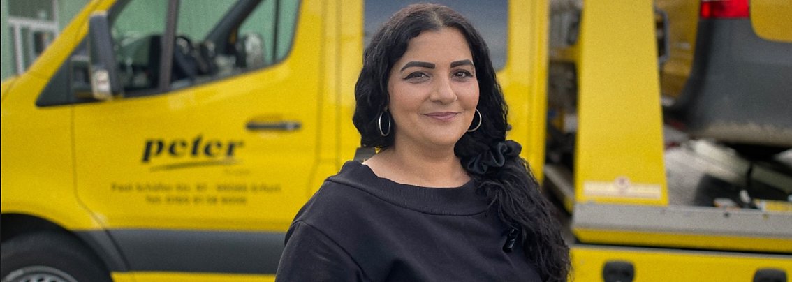 Eine Frau mit langen dunklen Haaren l&auml;chelt in die Kamera. Sie steht vor einem gelben ADAC Fahrzeug.