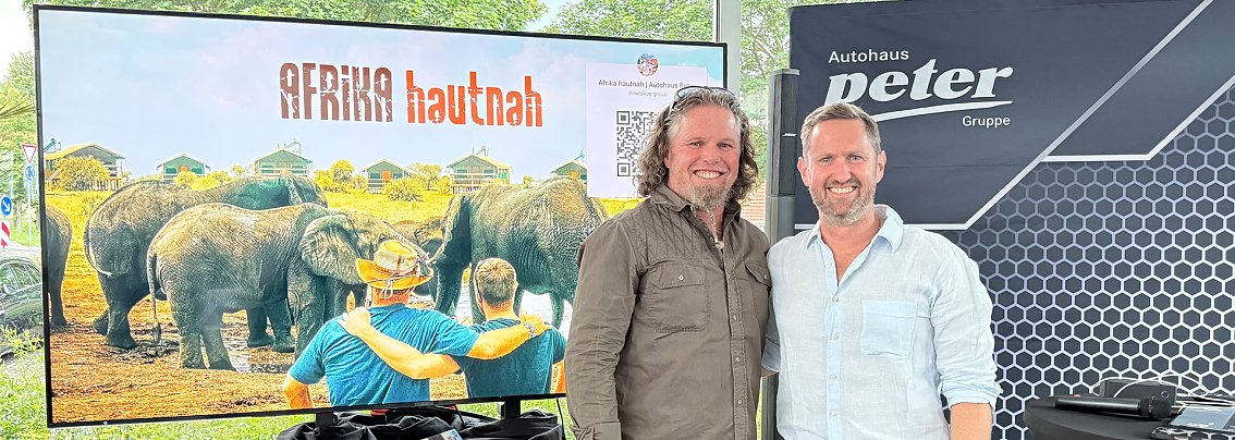 Guide Hannu und sein Begleiter Patrick vor Bildschirm mit Afrika-Motiv 