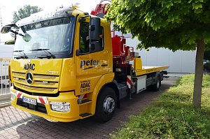 Gelber ADAC-Abschleppwagen mit Mercedes-Stern und der Aufschrift Autohaus Peter an der Seite, geparkt neben einem Baum und Geb&auml;uden, mit rotem Kranaufbau hinten.