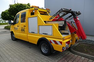 Gelbes ADAC-Servicefahrzeug des Autohaus Peter mit Abschleppvorrichtung, Seitenf&auml;chern und rotem Hebearm, geparkt auf einem gepflasterten Hof vor einer grauen Geb&auml;udewand.
