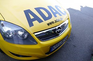 Vorderansicht eines gelben Opel-Fahrzeugs mit großem ADAC-Schriftzug auf der Motorhaube und der Webadresse www.adac.de. Das Auto steht auf Asphalt.