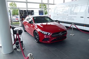 Roter Mercedes-Benz im Autohaus-Ausstellungsraum in Heiligenstadt. Das Fahrzeug ist mit roten Absperrseilen umrandet. Im Hintergrund ein gro&szlig;er wei&szlig;er Transporter und Farbmuster. Gro&szlig;e Fensterfronten lassen viel Tageslicht herein.