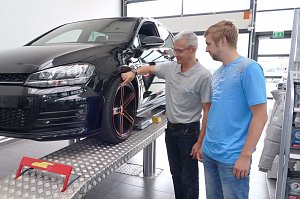 Mitarbeiter in der Werkstatt des �koda Autohauses erklärt einem Kunden die Profiltiefe eines Reifens an einem schwarzen Auto auf der Hebebühne.