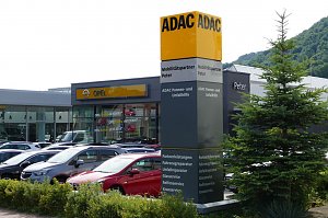 ADAC-Mobilitätspartner-Standort mit Autohaus Peter und Opel-Autohaus im Hintergrund. Vor dem Gebäude steht eine große, auffällige ADAC-Stele mit gelb-schwarzer Beschriftung und Serviceangaben. Davor parken zahlreiche Fahrzeuge. Rechts im Bild ist ein Baum.