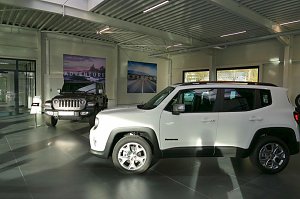 Heller Showroom mit einem wei&szlig;en Jeep Renegade im Vordergrund und einem schwarzen Jeep Wrangler im Hintergrund, Poster mit Landschaftsmotiven an der Wand.
