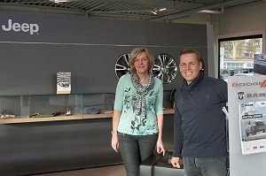 Christel Lauterbach und Danny Kindervater vom Jeep-Team stehen l&auml;chelnd vor dem Wartebereich im Jeep-Autohaus; im Hintergrund Wand mit Jeep-Logo und Felgen.