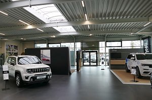 Innenraum eines modernen Jeep-Autohauses mit zwei ausgestellten wei&szlig;en SUV-Modellen, gro&szlig;en Glasfronten und heller, offener Architektur.