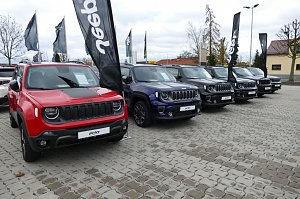 Reihe von Jeep-Fahrzeugen (Renegade-Modelle) auf dem Au&szlig;engel&auml;nde des Autohauses; im Vordergrund ein roter Jeep, daneben ein blauer, mehrere graue und schwarze Fahrzeuge, mit Jeep-Fahnen im Hintergrund.