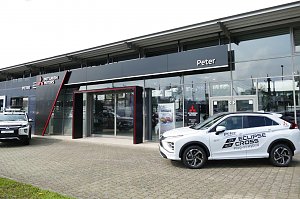 Eingangsbereich des Peter-Mehrmarkenhauses in G&ouml;ttingen mit Mitsubishi-Logo, einem wei&szlig;en Mitsubishi Eclipse Cross Plug-in Hybrid und einem weiteren Mitsubishi-Pickup vor dem Geb&auml;ude.