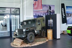 Historischer Jeep Willy in nostalgischer Pr&auml;sentation im Showroom mit US-Flagge und Jeep-Banner im Hintergrund.