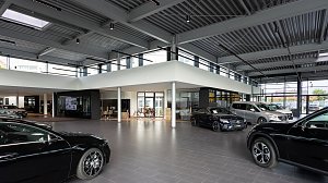 Heller Mercedes-Benz Schauraum mit mehreren ausgestellten Fahrzeugen, moderner Architektur, gro&szlig;en Glasfronten und industriellem Deckenstil.