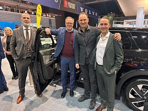 Vier M&auml;nner (u.a. Mario Voigt und Andreas Peter) stehen l&auml;chelnd neben einem schwarzen Auto mit ge&ouml;ffneter T&uuml;r. Im Hintergrund sind die Logos von Opel, Volvo und Renault Trucks auf Bannern zu erkennen.