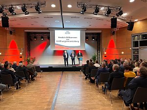 Auf einer gro&szlig;en Leinwand steht Die Automobilmesse Erfurt 2025 ist er&ouml;ffnet!. Davor sprechen drei M&auml;nner (rechts Helmut Peter) auf einer B&uuml;hne, w&auml;hrend zahlreiche Besucher im Saal zuh&ouml;ren.