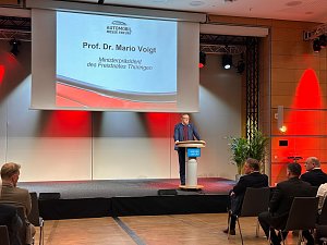 Prof. Dr. Mario Voigt spricht am Rednerpult der Messe Erfurt, im Hintergrund eine Leinwand mit seinem Namen und Titel als Ministerpr&auml;sident Th&uuml;ringens.