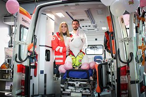 Ein ge&ouml;ffneter Rettungswagen steht im Autohaus. Zwei Mitarbeitende des Deutschen Roten Kreuzes stehen darin, vor ihnen sitzt ein gro&szlig;es Stoff-Einhorn auf einer Krankentrage. Rosa Luftballons schm&uuml;cken den Wagen.