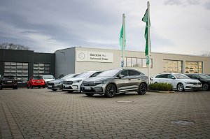 Mehrere �koda-Fahrzeuge stehen vor dem Geb&auml;ude �koda Plus Autowelt Peter. Zwei gr&uuml;ne Fahnen wehen im Vordergrund. Links im Bild parken weitere Autos.