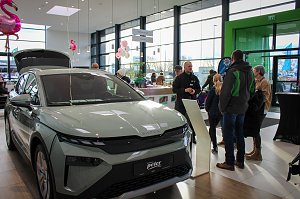 Ein neues �koda-Fahrzeug mit ge&ouml;ffnetem Kofferraum steht im hellen Showroom. Besucher unterhalten sich daneben, rosa Flamingo-Dekorationen h&auml;ngen von der Decke.