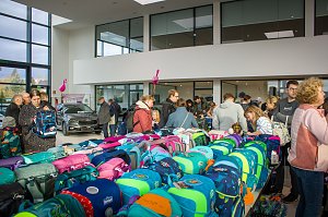 Viele Besucher stehen an Tischen voller bunter Schulranzen. Im Hintergrund ist ein schwarzes �koda-Fahrzeug ausgestellt, rosa Flamingos h&auml;ngen von der Decke.