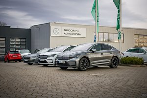 Mehrere �koda-Fahrzeuge stehen vor dem Geb&auml;ude �koda Plus Autowelt Peter. Zwei gr&uuml;ne Fahnen wehen im Vordergrund. Links im Bild parken weitere Autos.