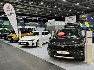 Ein schwarzer und ein wei&szlig;er Suzuki stehen nebeneinander. Im Hintergrund weitere Autos verschiedener Marken unter Peter-Bannern.