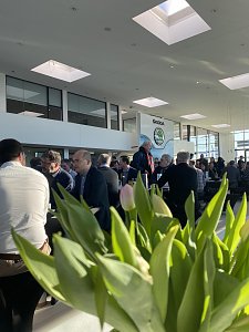 Innenaufnahme des Autohauses mit vielen G&auml;sten, die an schwarzen Tischen sitzen. Im Vordergrund unscharfe Tulpen, im Hintergrund gro&szlig;e Fenster und das Skoda-Logo.
