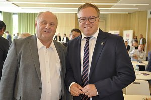 Das Bild zeigt links Gesch&auml;ftsf&uuml;hrer Helmut Peter und rechts Mario Voigt. Beide stehen nebeneinander in einem Konferenzraum, l&auml;cheln in die Kamera und tragen Anz&uuml;ge. Im Hintergrund sind weitere Personen an Tischen zu sehen.