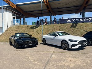  Zwei Mercedes-Benz Cabriolets, eines schwarz und eines wei&szlig;, stehen nebeneinander auf einem befestigten Platz beim Leichtathletik-Meeting Anhalt 2025. Hinter den Fahrzeugen verl&auml;uft ein Grashang mit Zuschauern und einer &uuml;berdachten Trib&uuml;ne.