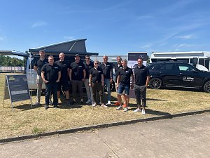 Gruppenfoto des Teams vom Autohaus Peter bei sonnigem Wetter. Zehn Personen stehen in schwarzer Teamkleidung mit Logo �Peter� nebeneinander vor einem silbernen Van und einem schwarzen Mercedes. Im Hintergrund sind ein Zelt, Werbebanner und weitere Fahrzeuge zu sehen. Alle l&auml;cheln in die Kamera.