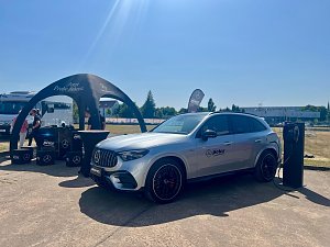Ein silberner Mercedes-Benz SUV des Autohauses Peter steht w&auml;hrend des Leichtathletik-Meetings Anhalt 2025 an einer mobilen Lades&auml;ule. Links befindet sich ein schwarzes Promotion-Zelt mit dem Schriftzug �Jetzt Probe fahren�, daneben mehrere Boxen und Mitarbeiter des Autohauses. Im Hintergrund sind Wohnmobile, B&auml;ume und ein sonniger, klarer Himmel zu sehen.