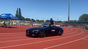 Ein schwarzes Mercedes-AMG Cabrio des Autohauses Peter f&auml;hrt mit einem Sportler &uuml;ber die Laufbahn im Stadion des Anhalt 2025 Leichtathletik-Meetings. Im Hintergrund sind das blaue Zelt der Stadtwerke Dessau, einige Zuschauer und die Beschilderung mit �WELCOME� und �BIENVENUE� zu sehen.