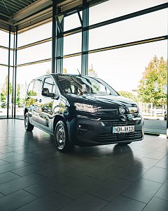 Ein schwarzer Opel-Transporter steht in einem hellen Autohaus mit gro&szlig;en Glasfenstern. 
