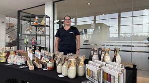 Stand mit regionalen Produkten im Autohaus Autowelt Peter. Eine Frau pr&auml;sentiert dekorative Gl&auml;ser mit Gew&uuml;rz- und Backmischungen, Flaschen und Geschenksets, die auf einem Tisch ausgestellt sind.