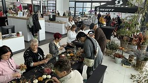 Besucherinnen und Besucher gestalten herbstliche Gestecke und Kr&auml;nze an Basteltischen im Autohaus Autowelt Peter. Auf den Tischen liegen K&uuml;rbisse, Zweige und Blumen. Im Hintergrund sind weitere St&auml;nde und ein Fahrradbereich mit SCOTT-Zelt zu sehen.