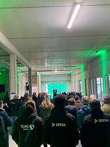Blick von hinten auf die R&auml;umlichkeit und die G&auml;ste, mehrere Personen tragen schwarze Jacken mit Dekra Logo.