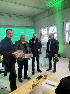 Andreas und Helmut Peter halten Pakete in den H&auml;nden und l&auml;cheln, daneben stehen 2 Herren von der Dekra