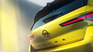 Nahaufnahme des gelben Fahrzeugs von hinten. Sichtbar sind die markanten, schmalen LED-R&uuml;ckleuchten, das Opel-Logo in der Mitte der Heckklappe und der Schriftzug ASTRA. Die Heckscheibe mit Spoiler und Scheibenwischer ragt &uuml;ber den oberen Bereich. Die Beleuchtung und leichte Unsch&auml;rfe erzeugen einen futuristischen Eindruck.