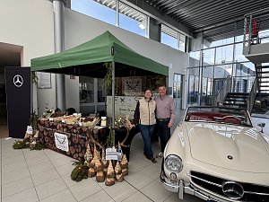 Der Stand vom Wildgourmet, bestehend aus einem grünen Pavillon und einem Stand mit Fleisch. Die Verkäufer stehen neben einem Mercedes-Benz Oldtimer.