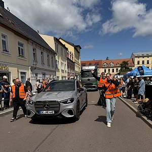 Man sieht einen grauen GLC und dahinter den grauen eActros. Neben dem GLC laufen 4 Radengel.