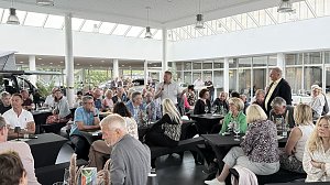 Autohaus mit vielen besetzten Tischen; eine Person spricht am Mikro.