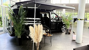 Schwarzer Mercedes Van mit Dachzelt/Vorzelt, daneben Palmen und afrikanische Deko.