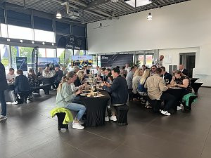 Szene im Peugeot-Autohaus: viele Personen sitzen an mehreren Tischen, während davor eine Person ins Mikrofon spricht.