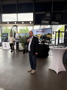 Eine Person steht vorn und spricht ins Mikrofon, im Hintergrund ein Bildschirm.