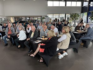 Szene im Peugeot-Autohaus: viele Personen sitzen an mehreren Tischen und hören gespannt zu.